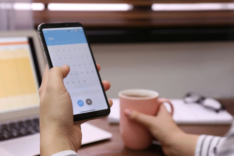 manage life apps A photo of a hand holding a smartphone with a calendar on the screen